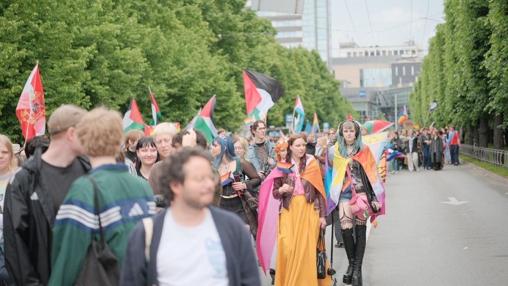 A crowd marches with palestinian flags on a tree-lined street.